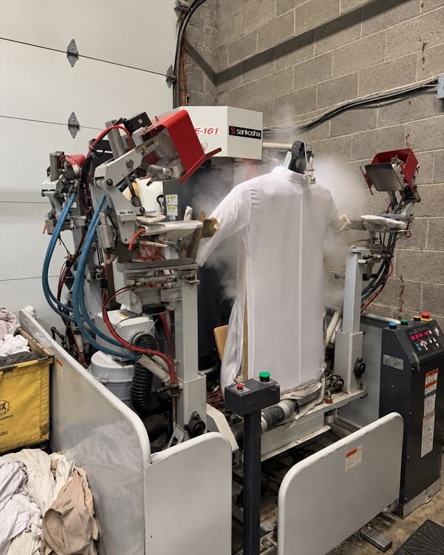 A white shirt on the steam press in the shop, steam rising around it.